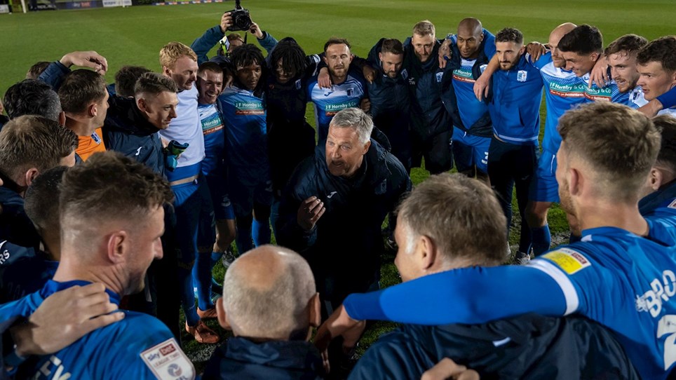 A photograph of Rob Kelly talking to the Barrow players and staff after victory at Forest Green Rovers