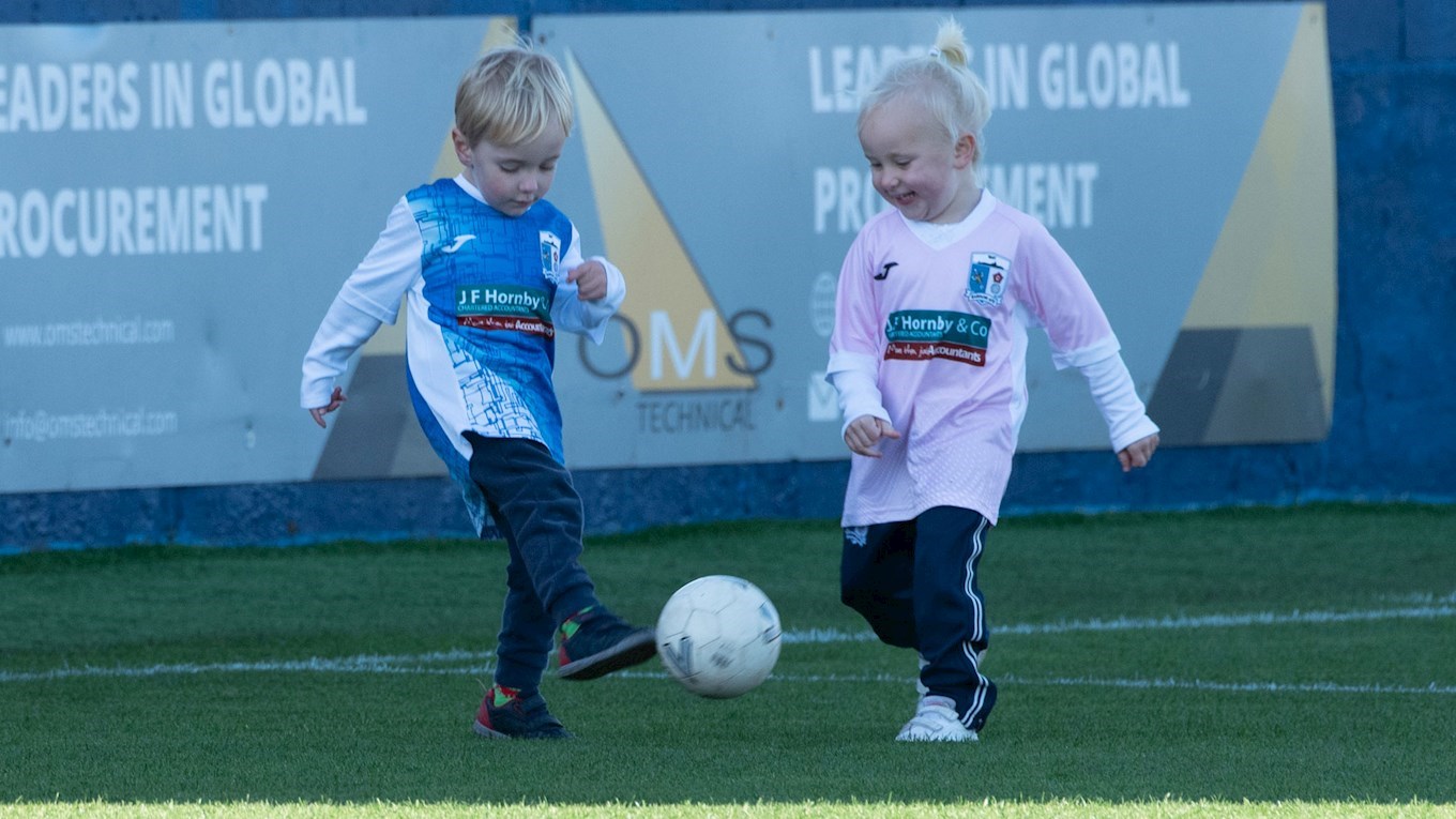 A photograph of two young mascots enjoying a kickabout on the pitch at Barrow