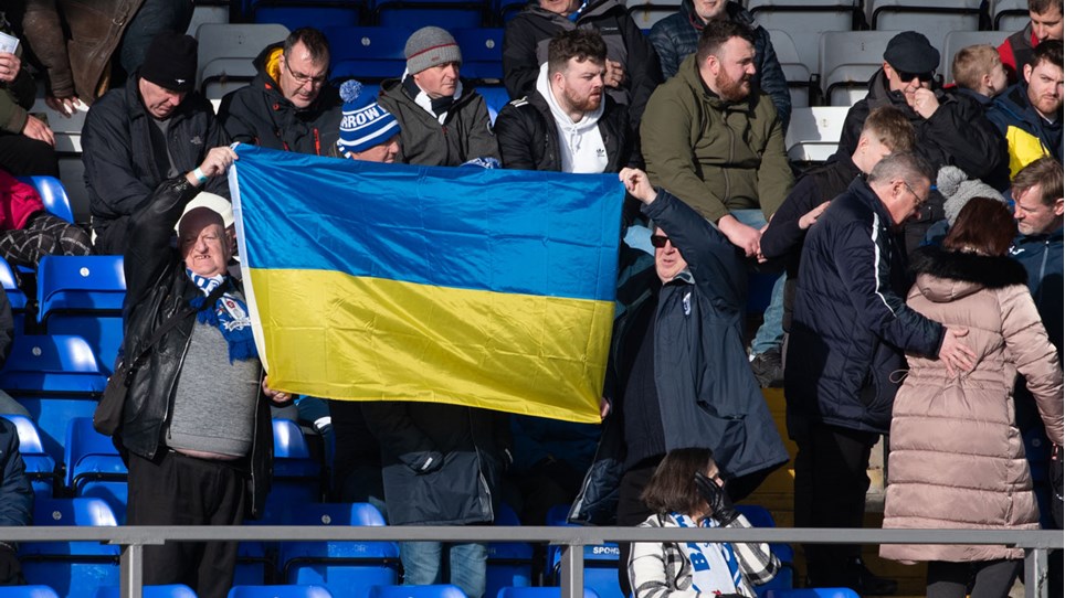 A photograph of Barrow fans holding up a flag of Ukraine ahead of the game against Harrogate Town