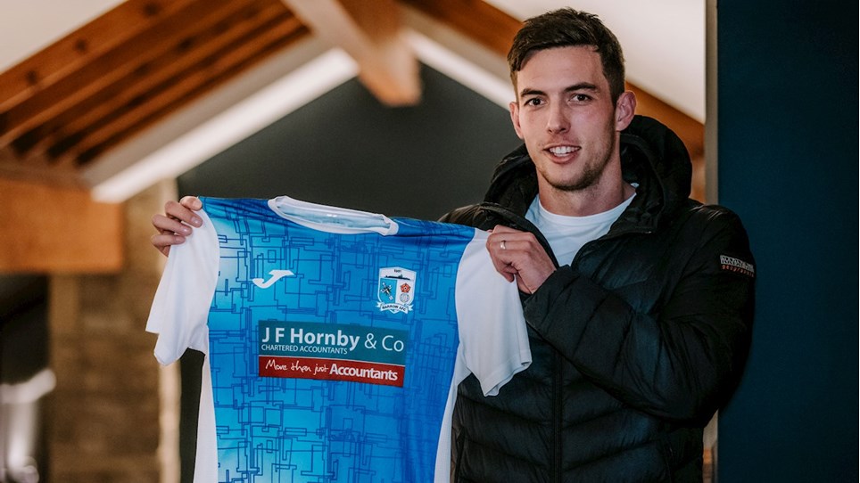 A photograph of Niall Canavan holding a Barrow shirt after completing his move from Bradford City