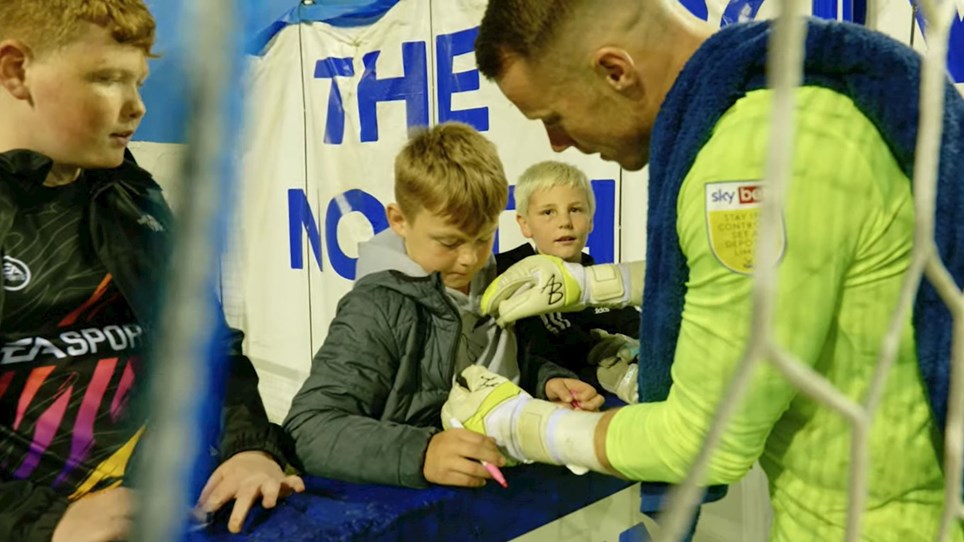 A photograph of Barrow goalkeeper Paul Farman signing an autograph for a young fan